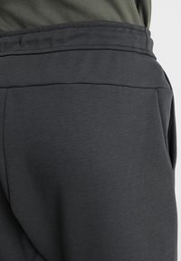 Mörkgrå svettbyxor med en slät yta, försedd med elastiskt midjeband och sidofickor, designad för komfort och funktionalitet.