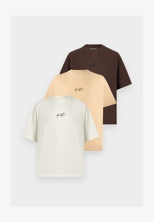 Trois t-shirts à manches courtes pliés en blanc, beige et marron foncé, chacun avec un petit logo noir "Your Turn" sur la poitrine.