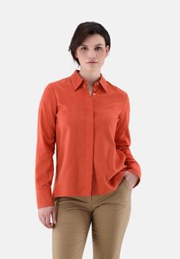Orange long-sleeve button-up shirt with a collar and smooth texture, paired with beige pants. Features a front pocket and classic fit.