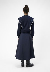 Navyblauwe outfit met een ribbeltruien met geborduurd schouderdetail en een lange rok. Laarzen maken de look compleet.