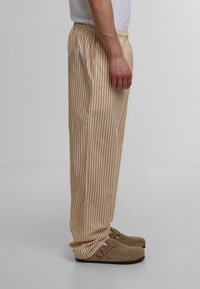 Bomull pysjamasbukser med vertikale beige og hvite striper, elastisk midje, sidelommer og en avslappet passform som strekker seg ned til anklene.