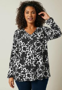 Chemise à boutons imprimée en noir et blanc avec un col en V, des manches longues et un motif abstrait. Tissu léger avec une coupe décontractée.