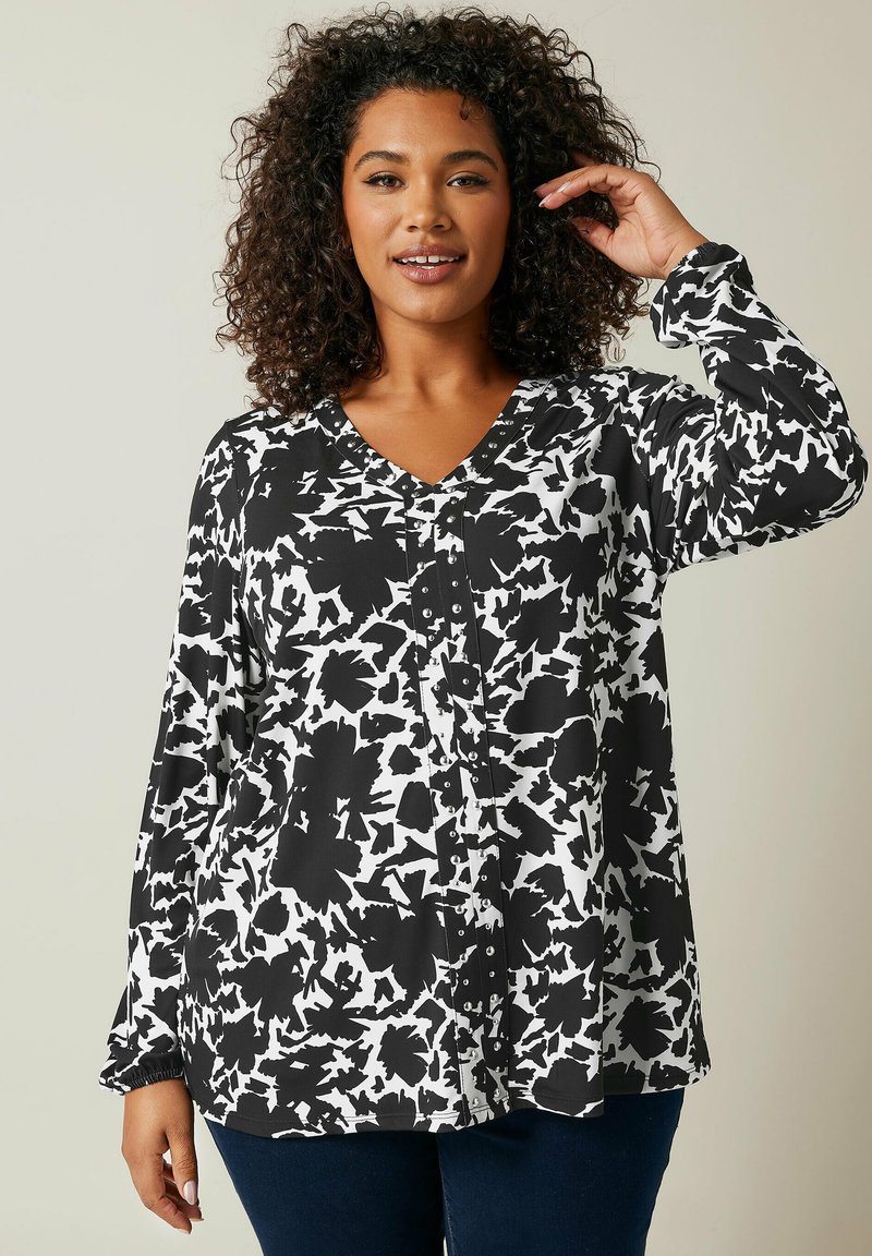 Chemise à boutons imprimée en noir et blanc avec un col en V, des manches longues et un motif abstrait. Tissu léger avec une coupe décontractée.