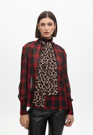 Blusa de cuadros rojos y negros con cuello alto y detalles de bufanda de leopardo; tela transparente; complementada con pantalones de cuero negros.