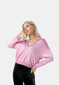 Maglione leggero rosa con scollo a V, spalle scese e polsini a costine. Abbinato a pantaloni neri lucidi.