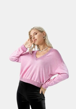 Maglione leggero rosa con scollo a V, spalle scese e polsini a costine. Abbinato a pantaloni neri lucidi.