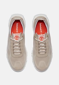Beige urheilukengät, joissa on verkkomateriaali päällä, valkoinen pohja ja tekstuuripinnat. Punainen sisäpohja, jossa on "Timberland"-logo. Kuusi reikää nauhoille.