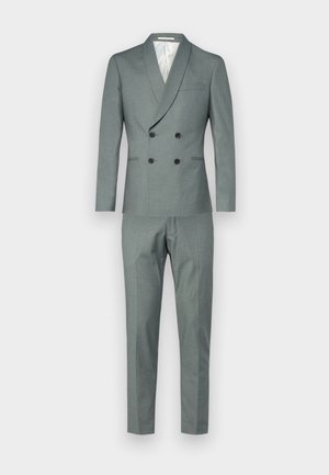 Traje de doble pecho en tejido gris claro, con solapa chal, dos bolsillos frontales y pantalones a medida a juego con un corte ajustado.
