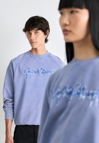 Lavendel crewneck sweatshirt med blå drippende tekst broderi, med en afslappet pasform og lange ærmer, parret med sorte bunde.