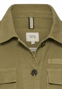 Khaki grøn skjorte med krave, to klaplomme, mørke knapper og et hvidt "Camel Active" mærke indeni halsudskæringen.