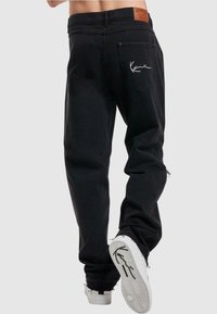 Pantalones de mezclilla negros con un fit relajado, que cuentan con un parche de cuero en la cintura, logo bordado en el bolsillo trasero y dobladillo desgastado.