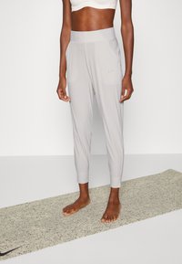 Ljusgråa träningsbyxor med en slim fit, tapered fållar, två sidofickor och en liten svart Nike-logga på vänster sida. Mjuk, slät textur.