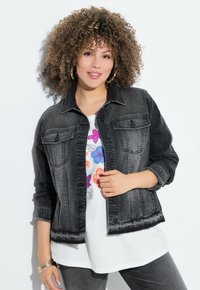 Mustat farkkutakki, jossa on kaksi rintataskua, kulunut helma ja revittyjen reunojen yksityiskohtia, käytetty valkoisen kukkakuosiset graafisen t-paidan päällä.