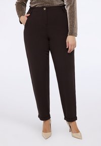 Braune, maßgeschneiderte Hosen mit Knopfverschluss, seitlichen Taschen und umgeschlagenen Säumen. Glatter Stoff, gerades Bein, kombiniert mit nudefarbenen Absätzen.