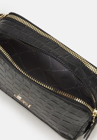 Portafoglio zip in pelle nera con motivo coccodrillo e dettagli dorati. L'interno presenta una fodera nera testurizzata con un sottile motivo geometrico.