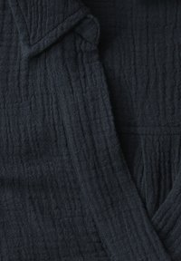 Tessuto texturizzato blu navy, con una superficie stropicciata e schemi di tessitura visibili; include un colletto e un design aperto davanti.