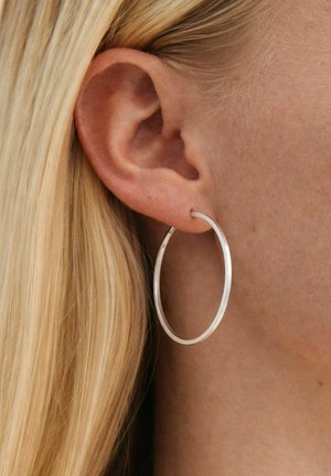 Bal oldali fül nagy ezüst karika fülbevalóval és fület mögött látható egyenes szőke hajjal.