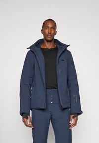 Giacca impermeabile color navale con cappuccio, dotata di cerniere e rivestimento in pile. Abbinate a pantaloni navy. Design elegante e funzionale.