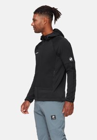 Czarna bluza z kapturem zapinana na zamek, z bocznymi kieszeniami i wzmocnionymi szwami, zestawiona z jasnoniebieskimi spodniami i naszywką z logo.