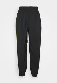 Černé sportovní kalhoty s elastickým pasem a manžetami, mají žluté pruhy po stranách a bílé panely s černým textem u kotníků.