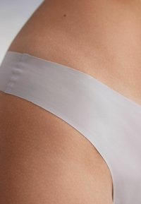 Sheer white thong, smooth texture, minimal design, soft waistband, featuring a seamless cut for discreet wear under clothing.