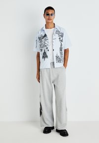 Short-sleeve shirt in light blue with black graphic prints, paired with gray wide-leg sweatpants and black chunky shoes. Sunglasses included.