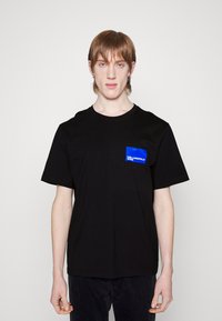 Melnas kokvilnas T-krekls ar īsām piedurknēm un apaļu kakla izgriezumu. Izceļas ar zilu kabatu, uz kuras redzams izcils "Karl Lagerfeld Jeans" logotips.