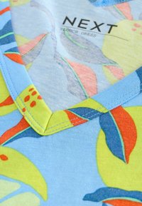 Robe décontractée en tissu bleu clair avec un motif floral coloré en jaune, vert et rouge. Décolleté en V avec des coutures contrastantes.