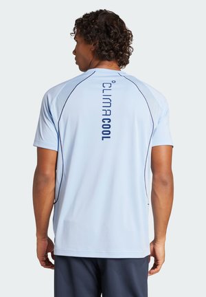 Hombre con cabello rizado vistiendo camiseta deportiva de manga corta azul claro con texto "climacool" en la espalda y pantalones cortos oscuros, de espaldas.