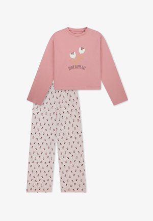 Mädchen steht barfuß, trägt ein pinkes Langarmshirt mit Blumen und Text und weiße Hosen mit kleinem Blumenmuster.