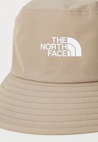 Cappello a secchi beige in tessuto, con una visiera ampia e strutturata, dettagli di cucitura verticale e logo "THE NORTH FACE" in bianco.