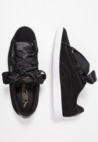 Baskets Puma en daim noir avec larges lacets en satin attachés en nœuds, semelles blanches et semelles intérieures "SoftFoam", vues de dessus et de profil.