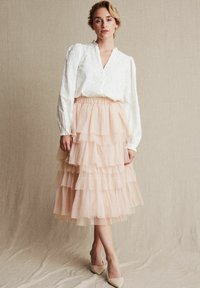 Hvid bluse med tekstureret blomsterdesign, lagdelt tylskørt i blush, knælangt, plisseret, parret med nude hæle.