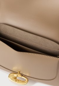 Béžová kožená kabelka s elegantným dizajnom, zlatými kovovými prvkami, magnetickým uzáverom a mäkkou textúrovanou vnútornou kapsou.