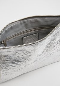 Silverfärgad metallisk dragkedjepåse med skräpad textur, grå satininsida och en liten logotypapplikation inuti.
