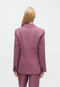 Lila maßgeschneiderter Blazer mit zusätzlicher Textur, einreihigem Design, Revers mit Kerb und schwarzen Knopfakzenten an den Ärmeln.