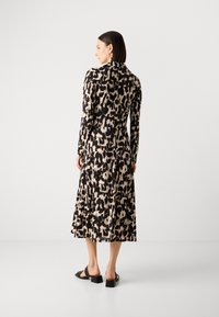 Abito con maniche lunghe, stampa animale nera e beige, realizzato in tessuto leggero, con gonna svasata e lunghezza fino al polpaccio, abbinato a sandali neri.