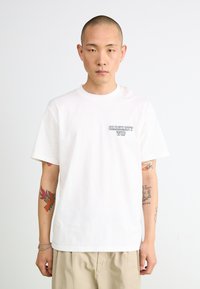 Maglietta bianca in cotone con un piccolo logo Carhartt WIP nero sul petto sinistro. Collo rotondo, maniche corte, vestibilità rilassata.