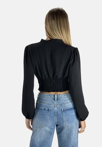 Schwarze kurz geschnittene Bluse mit gerafftem Rücken, langen Ärmeln und klassischem Kragen, kombiniert mit blauen, hoch taillierten Jeans.