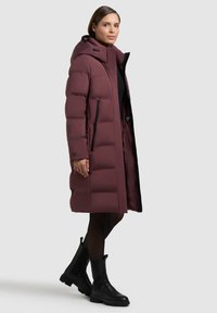 Burgundia värvi puffer-mantel kapuutsiga, millel on kappitud muster, küljetaskud tõmblukkudega ja must sisemine vooder. Välimuse täiendab mustad pahkluu saapad.