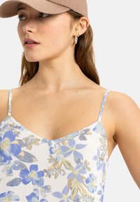 Camiseta sin mangas floral con tirantes finos, presenta un fondo claro con patrones de flores en azul y amarillo, hecha de una tela suave y liviana.