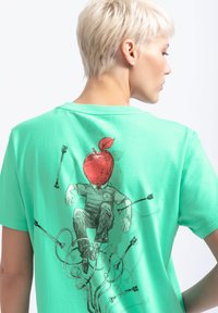 Mintgroene t-shirt met korte mouwen met een grafische illustratie van een figuur met een rode appel als hoofd, omringd door geïllustreerde kabels.