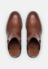 Scarpe slip-on in pelle marrone con pannelli elastici laterali, superficie liscia, punta arrotondata e accenti scuri contrastanti sui lati.