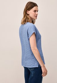 Top azzurro chiaro con texture, dal taglio morbido, maniche corte e spacchi laterali; realizzato in un morbido tessuto stropicciato, adatto per un abbigliamento casual.