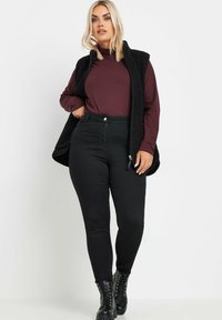 Czarna polarowa kamizelka nałożona na bordowy długi rękaw, w połączeniu z czarnymi obcisłymi dżinsami i czarnymi lace-up botkami za kostkę.