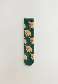 Calcetines verdes con un patrón repetido de criaturas de dibujos animados beiges con cuernos y bufandas rojas. Textura suave, longitud estándar, diseño de punto.