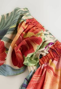 Ceinture élastique avec tissu floral froncé et à volants présentant de grands motifs botaniques rouges, orange, verts et violets sur un matériau léger.