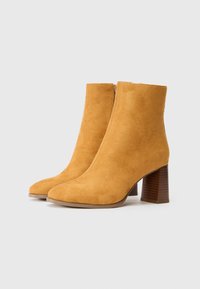 Helle Wildleder-Stiefeletten mit spitzem Zehenbereich und einem klobigen, hölzernen Blockabsatz. Verfügt über einen glatten Reißverschluss auf der Rückseite für einfaches Anziehen.