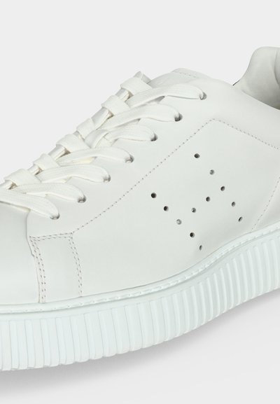 Baskets en cuir blanc avec lacets blancs, trous de ventilation perforés sur le côté et semelle épaisse en caoutchouc nervurée.