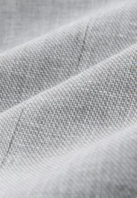 Tissu gris clair avec un motif de tissage texturé serré à petite échelle et des coutures visibles le long des plis.